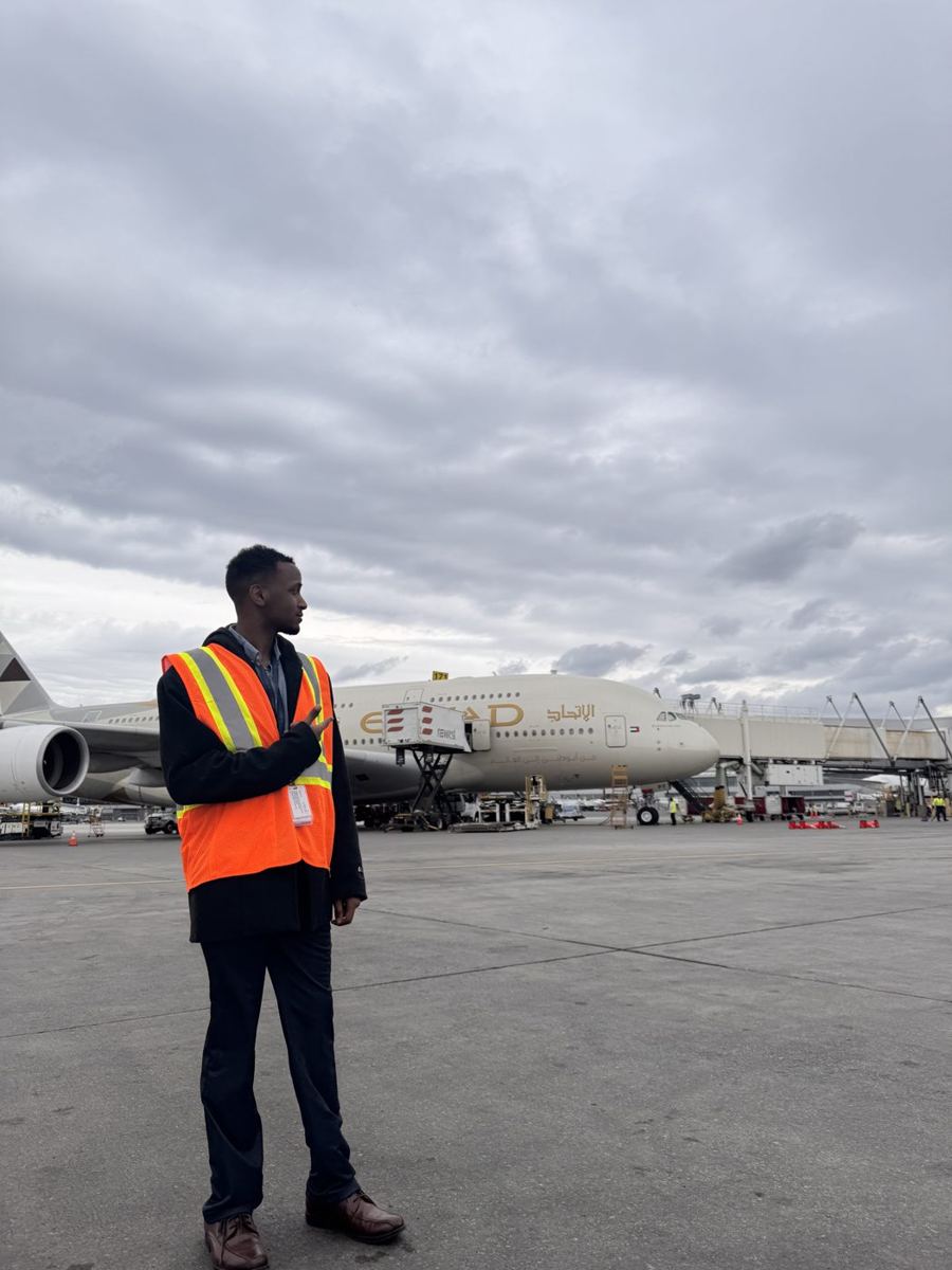 Rayan in a hi-vis vest on the airfield in front of a large passenger jet