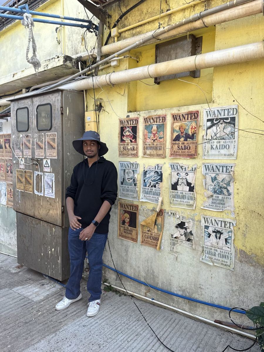 Rayan standing beside a yellow wall covered in anime wanted posters